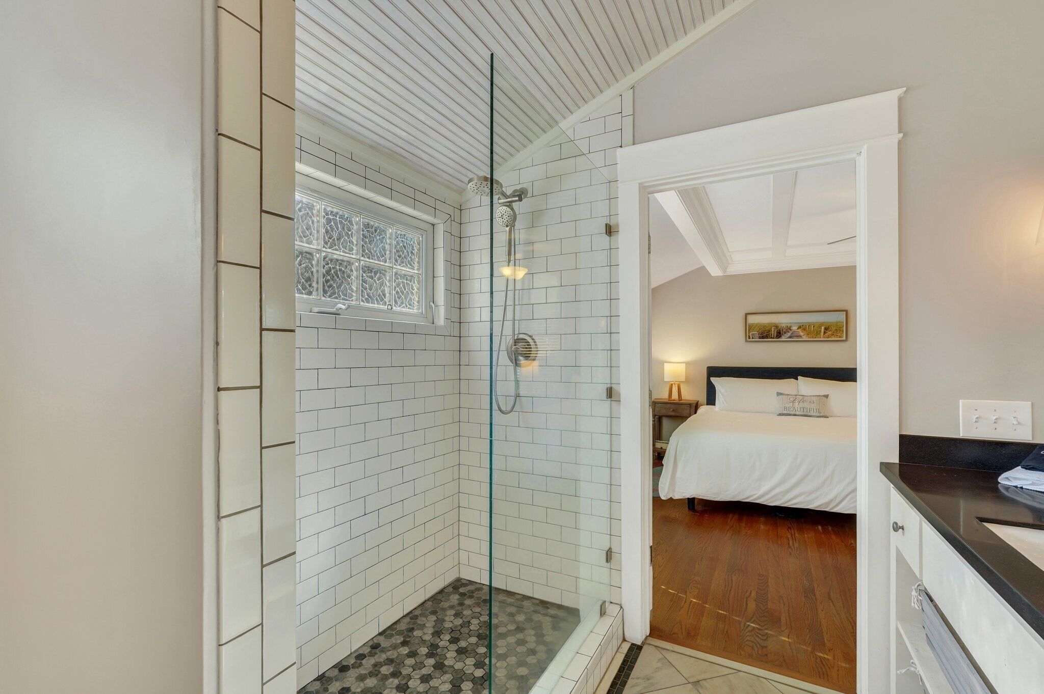 Une salle de bain moderne avec une douche à parois de verre, des murs recouverts de carreaux blancs et un plancher en bois.