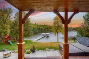 A covered patio with a view of a lake, a wooden play structure, and a dock extending into the water. - Stunning Lakefront Retreat with Hot Tub & Fishing Paradise (Tower)