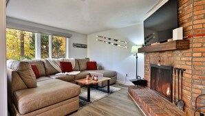 Una sala de estar moderna con un sofá modular, una chimenea y un ventanal con vistas a árboles.