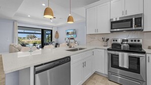 A modern kitchen with white cabinetry, stainless steel appliances, and a large island with a dishwasher. - Brand New & Luxurious, Sunsets, Heated Pool & Spa - Villa Palm Breeze - Roelens (Cape Coral)