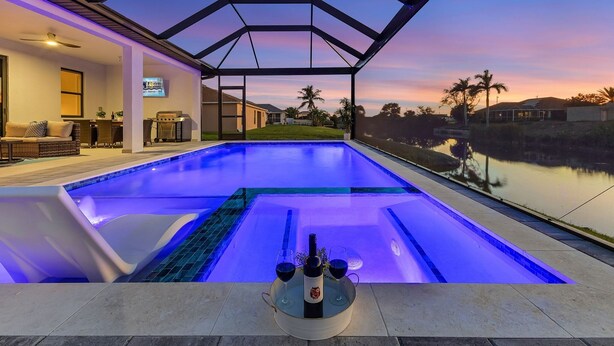 A swimming pool with a glass enclosure and a sunset view. - Brand New & Luxurious, Sunsets, Heated Pool & Spa - Villa Palm Breeze - Roelens (Cape Coral)