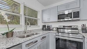 A modern kitchen with stainless steel appliances, a granite countertop, and white cabinetry. - Gulf Access, Dock, Heated Pool, Across from the Beach - Sea-cluded Bungalow -Roelens (Fort Myers Beach)
