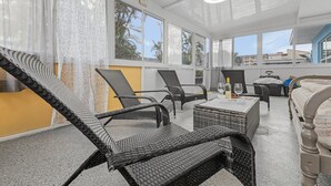 A room with wicker furniture, a bed, and large windows. - Gulf Access, Dock, Heated Pool, Across from the Beach - Sea-cluded Bungalow -Roelens (Fort Myers Beach)