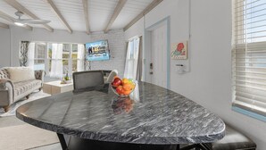 A spacious room with a marble dining table, a bowl of fruit, a sofa, and a ceiling fan. - Gulf Access, Dock, Heated Pool, Across from the Beach - Sea-cluded Bungalow -Roelens (Fort Myers Beach)