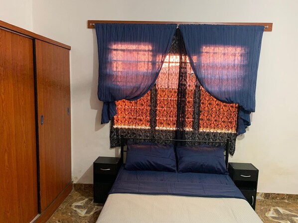 A bedroom with a bed, a wardrobe, and a window with patterned curtains.