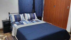A bedroom with a bed, a nightstand, a wooden wardrobe, and a patterned rug.