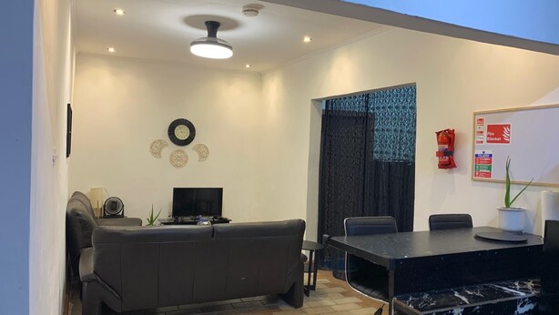 A modern living room with a sofa, a TV, a ceiling fan, and a dining area with a table and chairs.