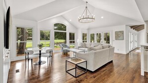 Een ruime woonkamer met een grote grijze modulaire bank, een ronde eettafel met stoelen en een kroonluchter.