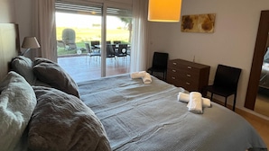 A bedroom with a large bed, a desk, and a chair. There is a sliding glass door leading to an outdoor area with chairs and a table. - Beautiful 2 Bed Apartment Mar Menor Golf Resort (Torre Pacheco)