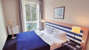 Une chambre d’hôtel avec un grand lit, une table de chevet avec une lampe, une fenêtre avec des rideaux et un tableau encadré au mur.