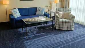 Une chambre d’hôtel avec un canapé bleu, un fauteuil à motifs écossais, une table basse en verre et un tableau encadré au mur.