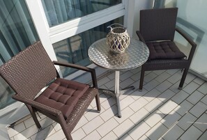 A balcony with two wicker chairs and a small round table, featuring a woven basket on the table.