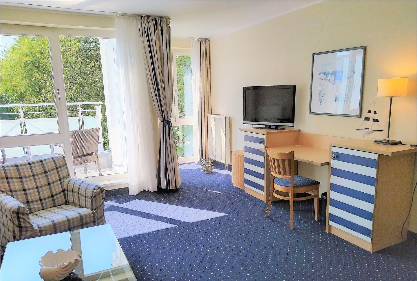 Ein Hotelzimmer mit Bett, Schreibtisch, Sessel, Fernseher und einem fenster mit Vorhängen.