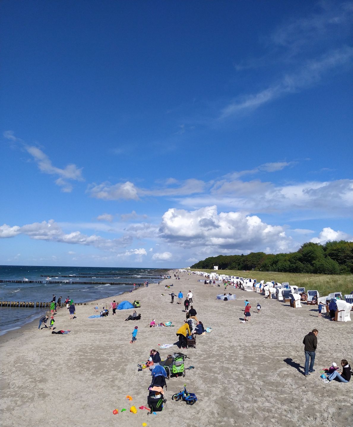 Una playa con gente, sillas de playa y cielo despejado.