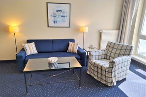 A room with a blue sofa, a plaid armchair, a glass coffee table, two floor lamps, and a framed picture on the wall. - "My time out" App. 202 - Private vacation apartment in a unique location directly on the (Zingst)