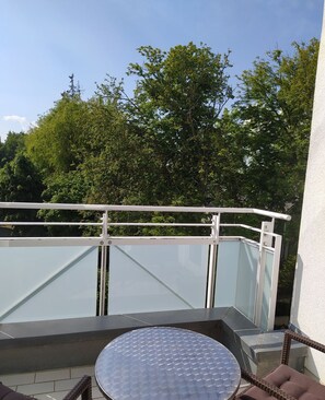 Ein Balkon mit Glastrennwand, einem runden Tisch und Korbmöbeln.
