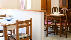 A dining area with wooden chairs and a table, a window with blinds, and a cabinet with books. - P044 - Porto Recanati, comfortable three-room apartment in the historic center (Porto Recanati)