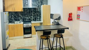 A compact kitchen with wooden cabinets, a stove, a sink, and a small bar area with stools.