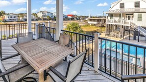 A wooden deck with a table and chairs, overlooking a swimming pool and a residential area with houses and a church. - Flew The Coop-Second Row Beach House Community (Garden City Beach)