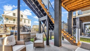 An outdoor patio area with wicker furniture, a grill, and a staircase leading to an upper level. - Flew The Coop-Second Row Beach House Community (Garden City Beach)