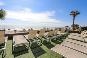 Eine Strandlounge mit Reihen von Liegestühlen, die zum Meer blicken, einer Palme und blauem Himmel.