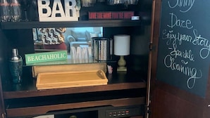 A wooden bar area with shelves holding various bottles and glasses, a chalkboard with motivational writing, and a sign that says "UNWIND UNPLUG RELAX". - Sunny Daze Walk to Beach 2 Decks Pet Friendly (Galveston)