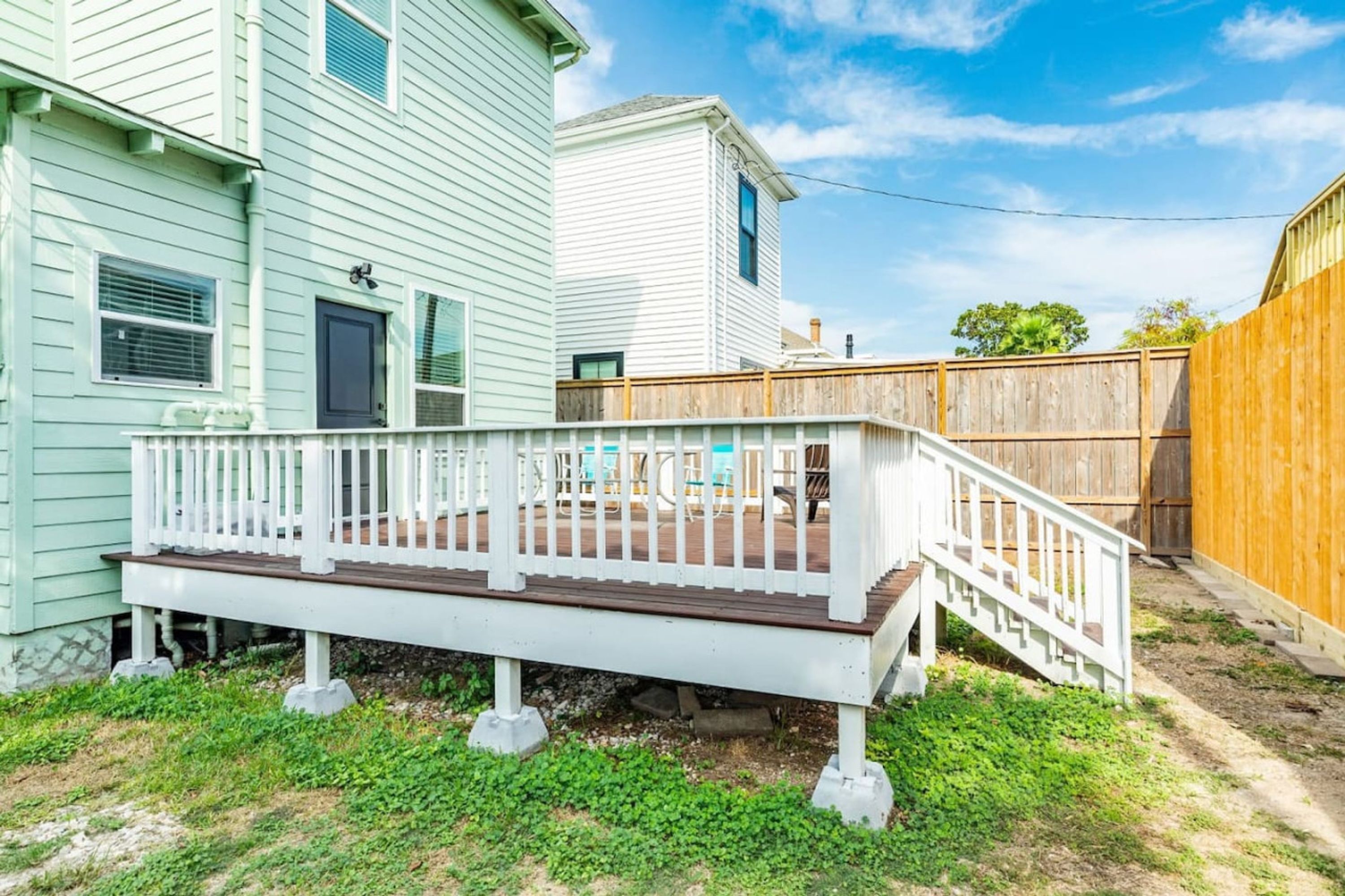 A wooden deck with a white railing, surrounded by a grassy yard and a wooden fence.