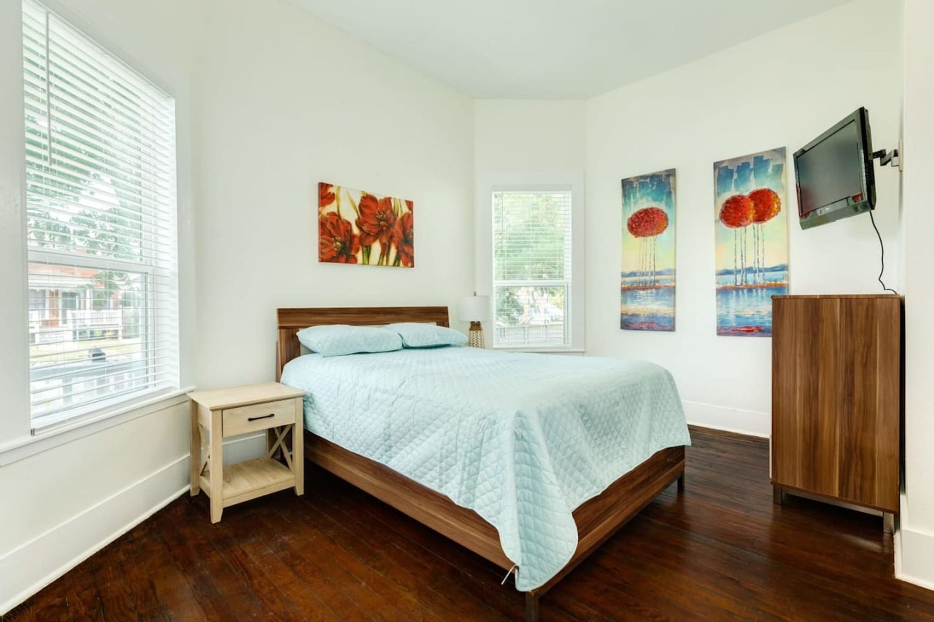 A bedroom with a bed, a nightstand, a wooden cabinet, and artwork on the walls.