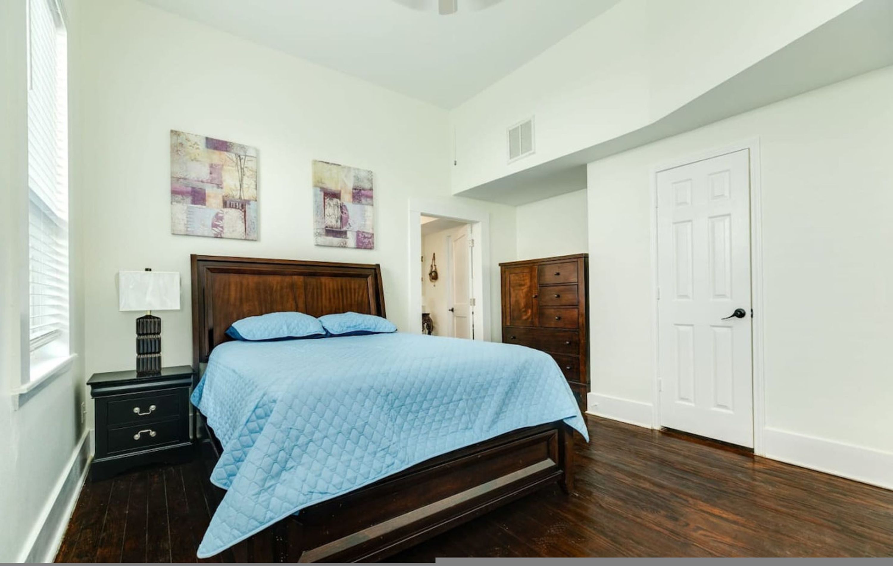 A bedroom with a wooden bed, a nightstand, a dresser, and two wall-mounted paintings.
