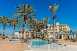 Ein Resort mit Poolanlage, umgeben von Palmen und einem mehrstöckigen Gebäude mit Balkonen.
