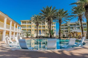 Poolbereich mit Liegestühlen, Palmen und einem mehrstöckigen Hotel im Hintergrund.