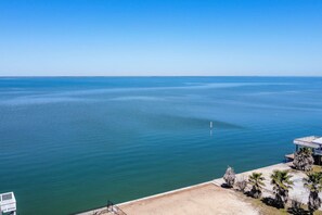 A coastal view with a clear sky, a sandy beach, and a building with a balcony overlooking the sea.