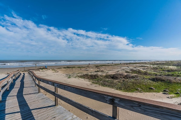 A wooden boardwalk leading to a beach with a clear sky.