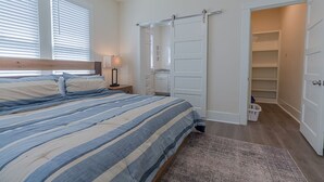 A bedroom with a bed, a nightstand, a lamp, a sliding door closet, and a view of a laundry basket.