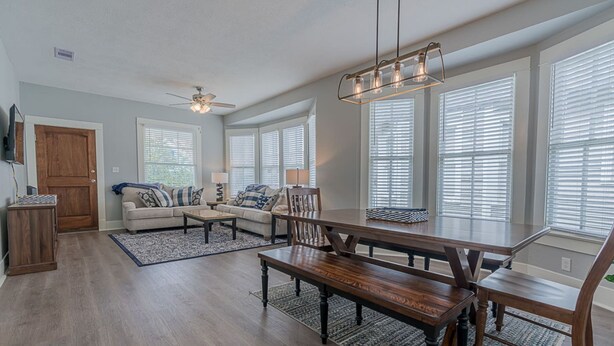 A spacious living room with a wooden dining table, two sofas, and a ceiling fan.