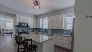 A modern kitchen with white cabinets, a granite island, and a built-in microwave.