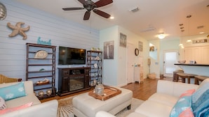 A living room with a TV, wooden shelves, and a ceiling fan. - Serenity By the Sea - Great Views in Treasure Isla (Freeport)