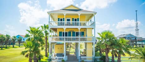 A two-story building with a balcony, surrounded by palm trees and a clear sky.