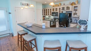 A kitchen with a central island, wooden stools, a microwave, a refrigerator, and a chalkboard sign. - Serenity By the Sea - Great Views in Treasure Isla (Freeport)