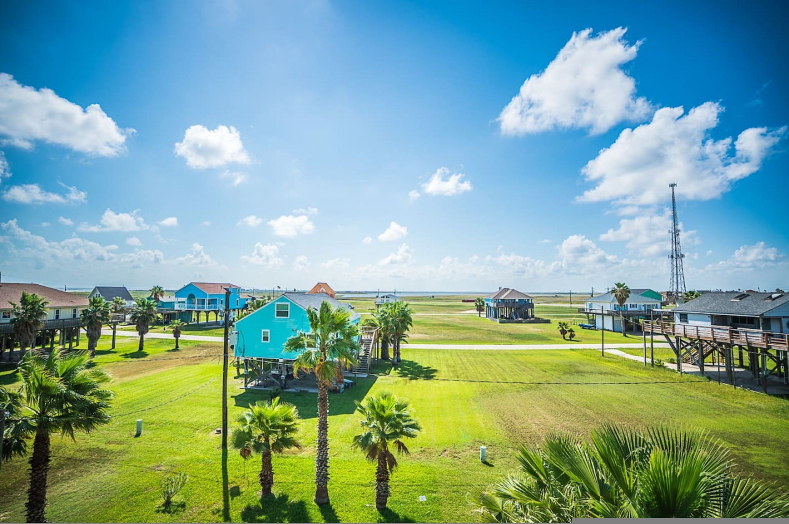 A coastal residential area with houses, palm trees, and a clear sky.