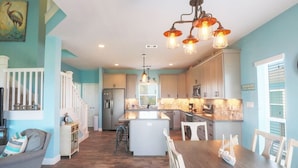 A spacious kitchen with a central island, white cabinetry, and a dining area with a wooden table and chairs. - Great bay Views and a Pool in Isla Del Sol (Galveston)