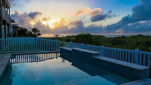 A swimming pool with a blue fence and a view of the ocean at sunset. - Great bay Views and a Pool in Isla Del Sol (Galveston)