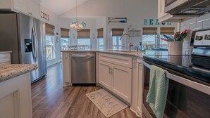 A modern kitchen with white cabinetry, stainless steel appliances, and a view of the beach. - The Coast is Clear Great Home By Beach Bay (Galveston)