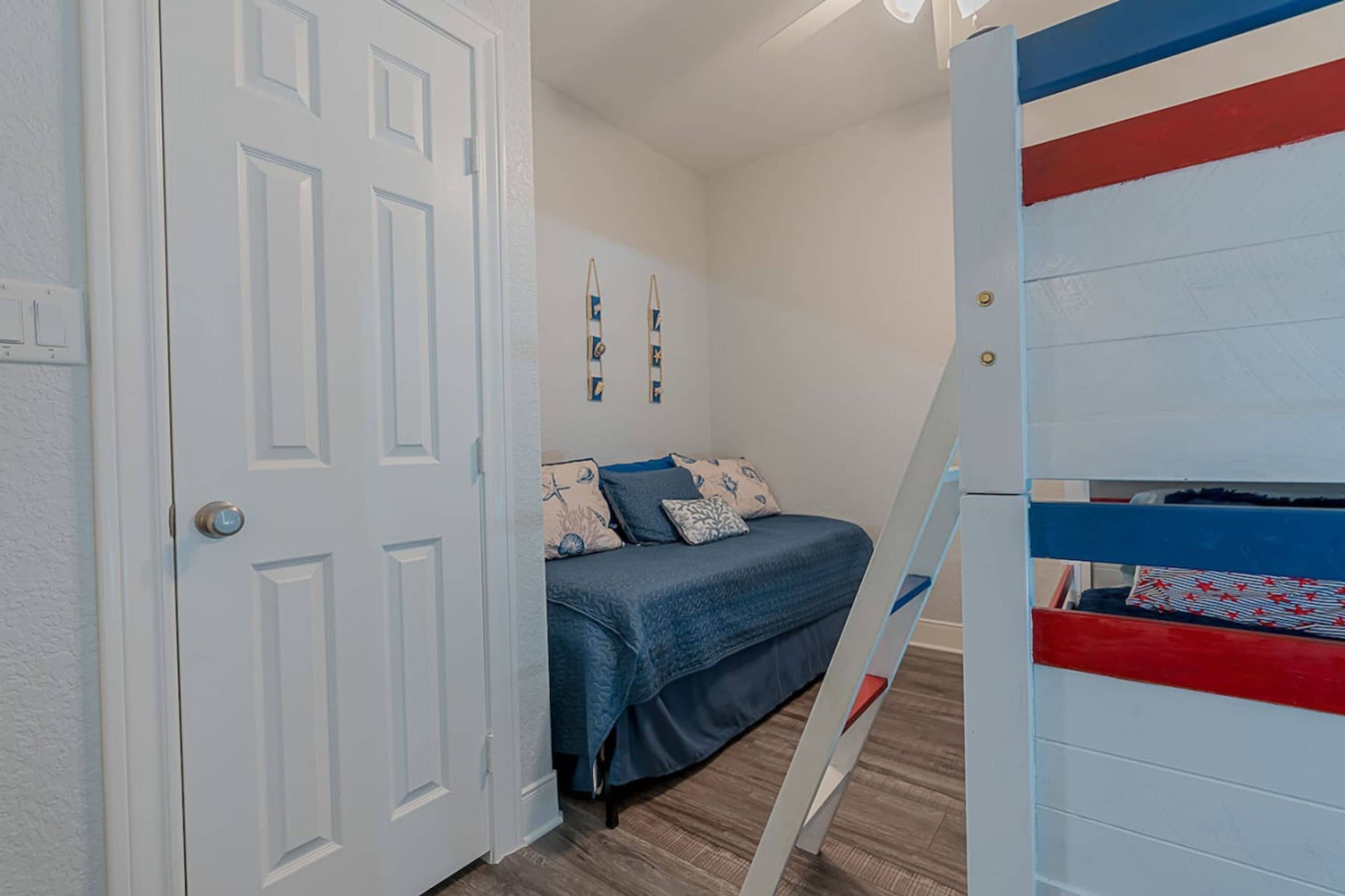 Un dormitorio con una cama, una puerta blanca y una cama litera con detalles en rojo y azul.