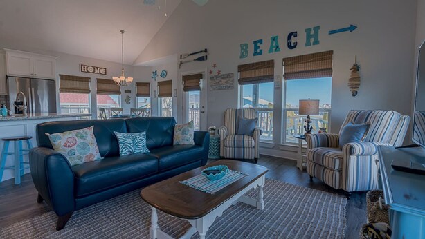 A living room with a blue sofa, striped armchairs, a wooden coffee table, and a kitchen in the background. - The Coast is Clear Great Home By Beach Bay (Galveston)