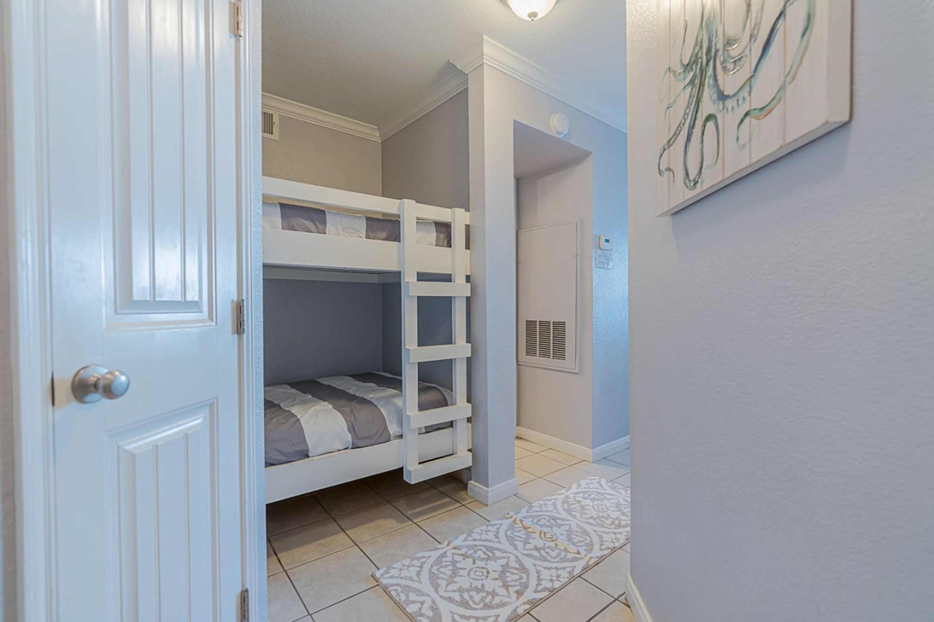 A room with bunk beds, a patterned rug, a door, and a wall with abstract art.