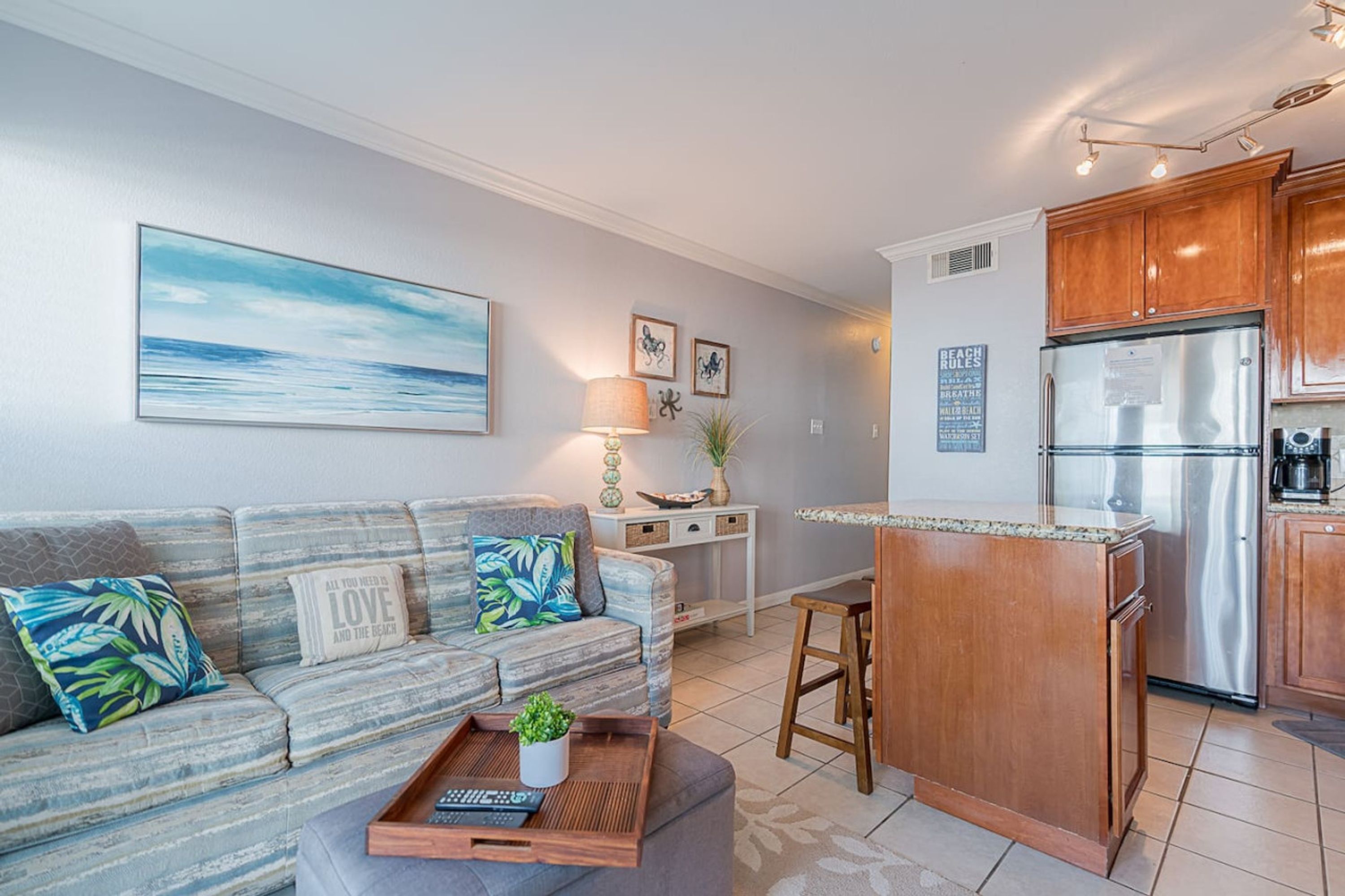 A modern living room with a sofa, a coffee table, and a kitchen area with wooden cabinets and a refrigerator.