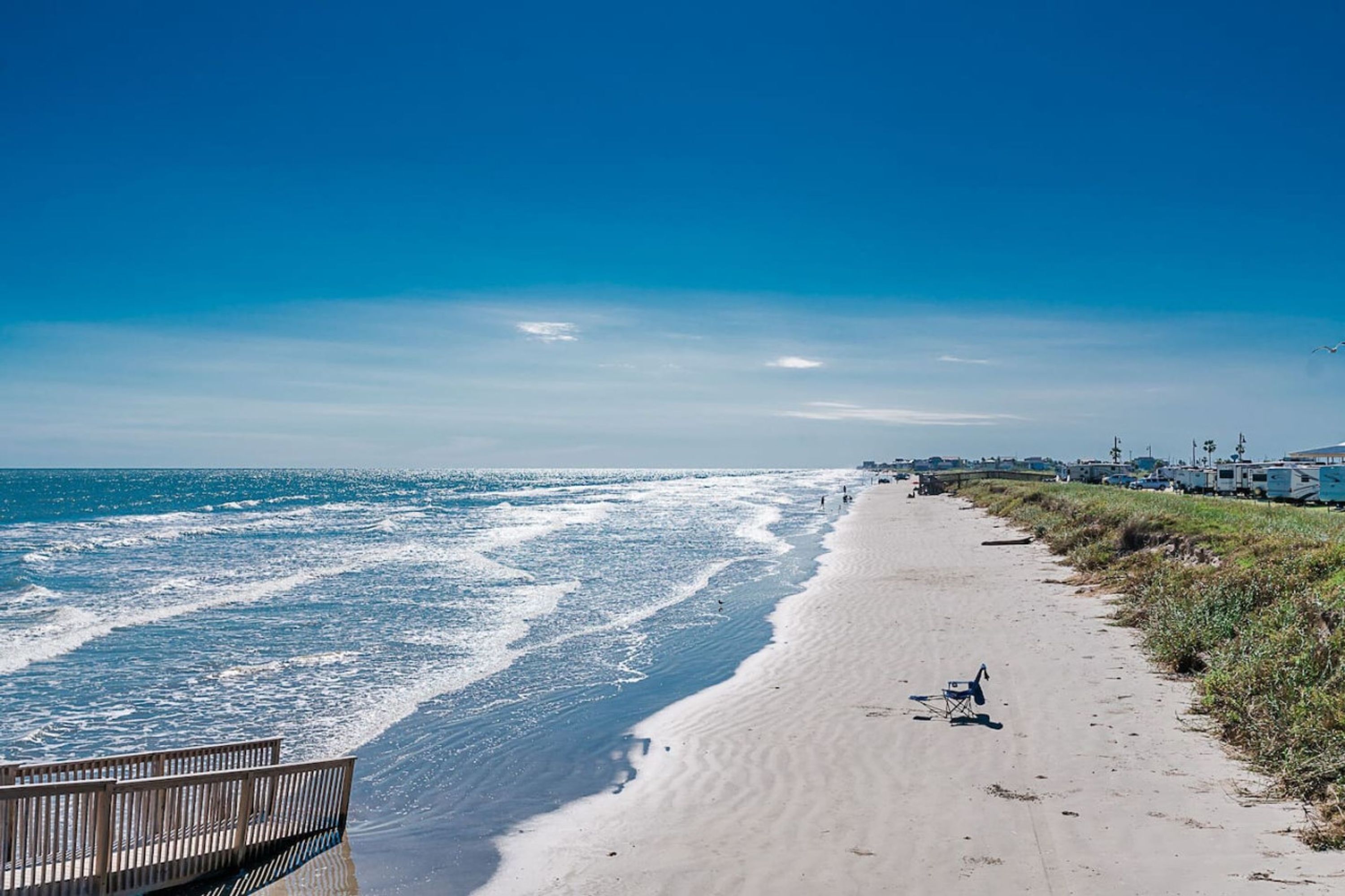A beach with a wooden walkway, a chair, and a row of RVs.
