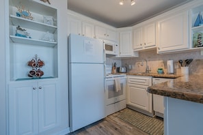 A modern kitchen with white cabinetry, a built-in microwave, and a granite countertop. - Get Beach Dazed in Galveston (Galveston)