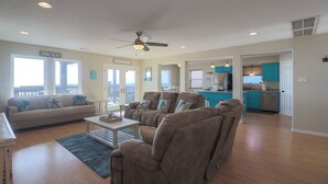 A spacious living room with a sofa, armchairs, and a coffee table. There is a kitchen area with teal cabinets and a dishwasher. - Superb Home With Private Walkover to Beach (Freeport)